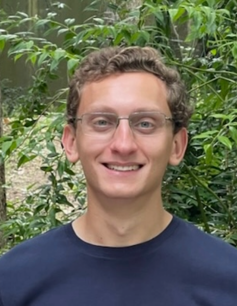 Man with brown hair wearing a dark blue shirt in a outdoor setting